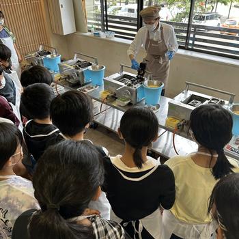 もみじ饅頭を作るために説明を聞く児童